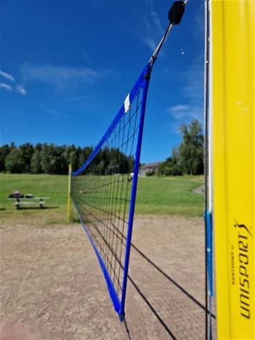 Alt-text: En volleybollplan vid Farstanäs Camping & Havsbad med ett uppsatt nät, omgiven av grönska och en strandliknande miljö.