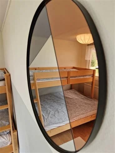 En oval spegel med träkant reflekterar dagsljus på Farstanäs camping & havsbad, vilket skapar en varm och inbjudande atmosfär.