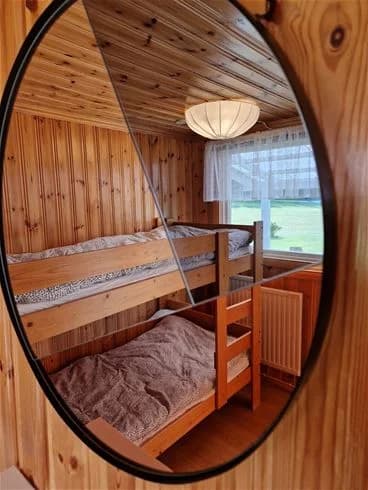 En träinredd sovrumsinteriör på Farstanäs Camping & Havsbad med en bekväm säng, bruna tränyanser i möbler och golv, samt mjuka sängkläder.