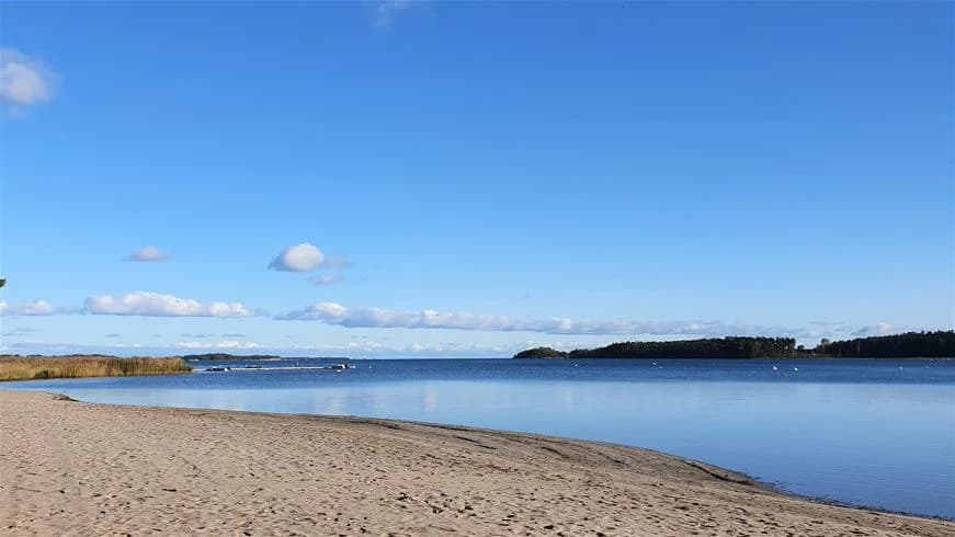 En vidsträckt sandstrand vid havet med blått vatten, en klar horisont och kustlinje, perfekta för sol och bad på Strandstuvikens havsbad & camping.