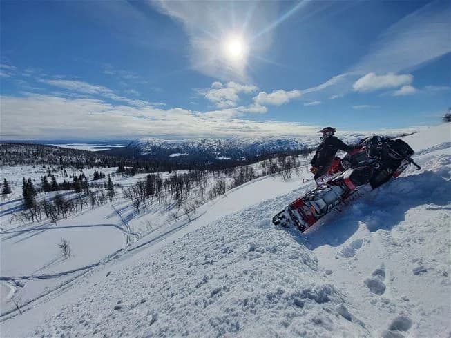 En snöig vinterlandskap med en snöskoter i förgrunden vid Jormvattnets fiskecamp. Omgiven av glaciala formationer, platsen erbjuder äventyr och rekreation i vintersportmiljö.