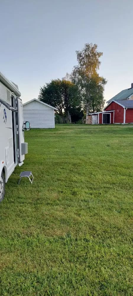 En grön gräsyta med husvagn och husbil parkerade på en campingplats. I bakgrunden syns ett öppet område med grönska, vilket tillhör Sangis motell och camping.