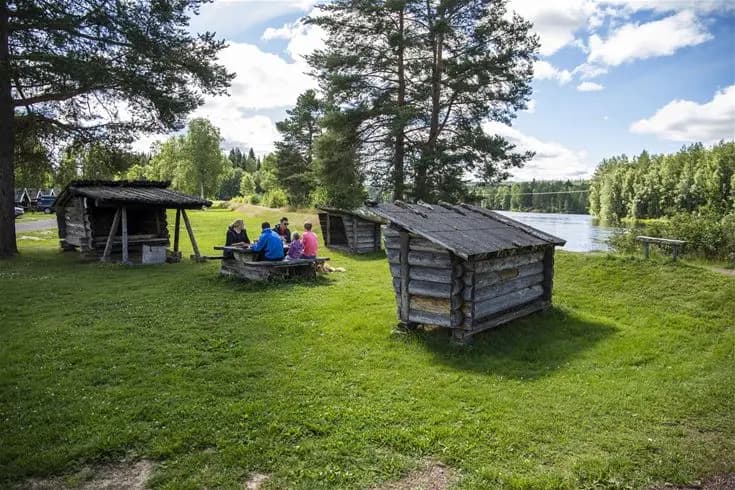 En mysig stuga vid Älvdalens camping omgiven av grönska och träd, med en gräsbevuxen äng i förgrunden.