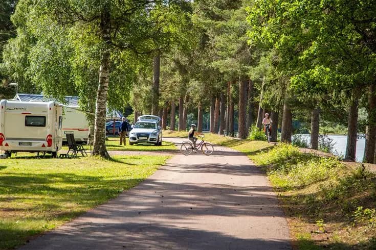 En cykel står parkerad på grusväg vid sidan av en tältplats omgiven av träd och grönska på Älvdalens camping.