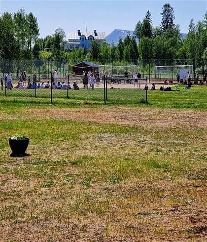 Bild av Hede Camping med grönskande gräsmatta och en inhägnad område. Människor promenerar och njuter av fritiden i parkliknande miljö.