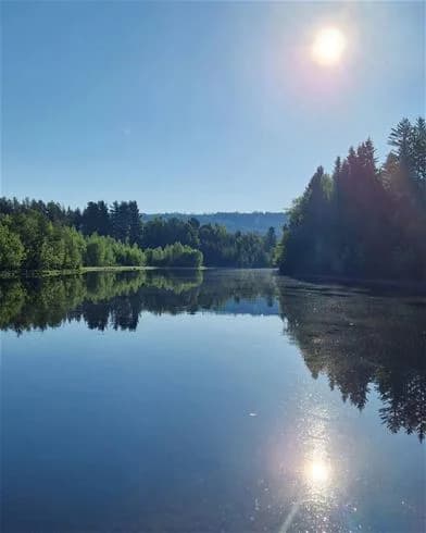 En bild av en klarblå himmel som speglas i ett stilla vattendrag, omgiven av grön natur, troligtvis vid Hede Camping.