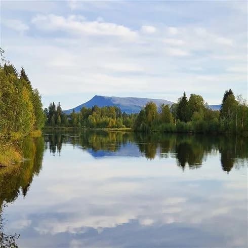 Vy över Hede Camping med en naturskön bakgrund av berg, vattendrag och molnig himmel.