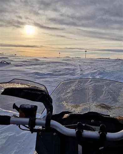 En motorcykel parkerad i snölandskap vid Hede Camping, med snö och is på marken och en spegel reflekterande vinteromgivningen i skymningen.