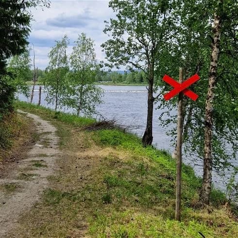 En naturskön vy över Hede Camping med omgivande vattenvägar och frodig grönska. Flodens strandlinje breder ut sig i förgrunden medan en vacker sjö och våtmarker kan skymtas i bakgrunden. En stig slingrar sig genom landskapet, perfekt för naturvandringar.