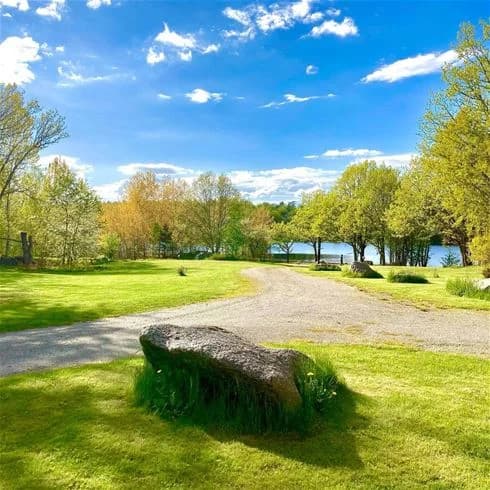 Sjöutsikt med blått vatten, omgiven av grönska och träd vid Långsjön Stugor & Camping.