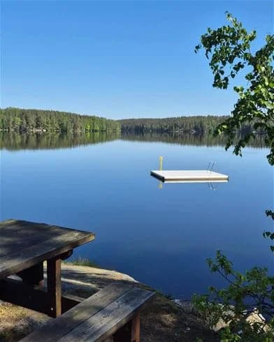 En naturskön sjö med brygga och omgivande grönska på Långsjön Stugor & Camping. Perfekt plats för friluftsliv och avkoppling vid vattnet.