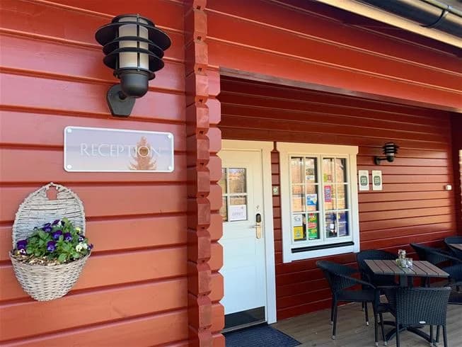 En trästuga vid Långsjön Stugor & Camping med träpanel, en trädörr och blomkrukor bredvid ingången.