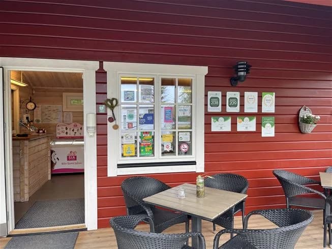 En mysig uteplats med träbord och stolar vid Långsjön Stugor & Camping, omgiven av träpanel och grönskande gårdsmiljö.