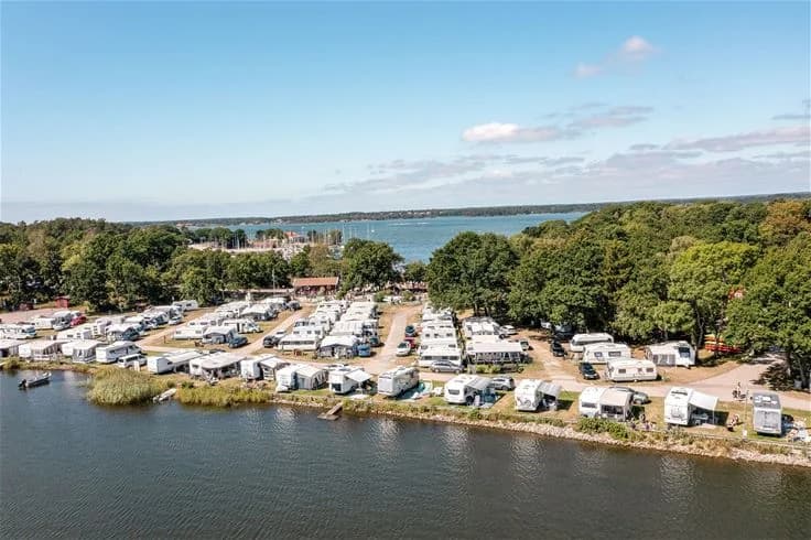 Flygbild över Dragsö camping & stugby som visar en kustlinje med sandstränder, ett vattenområde och gröna naturområden.