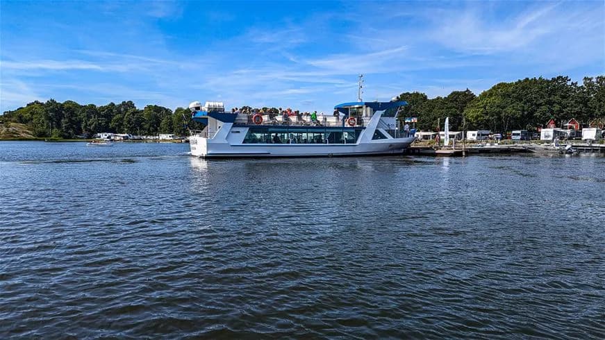 En färgglad bild av en vacker sjö där flera båtar ligger förtöjda vid en brygga. Stillsam atmosfär med vita moln som speglas i det blå vattnet vid Dragsö Camping & Stugby. Perfekt för en avkopplande utomhusdag nära naturen.
