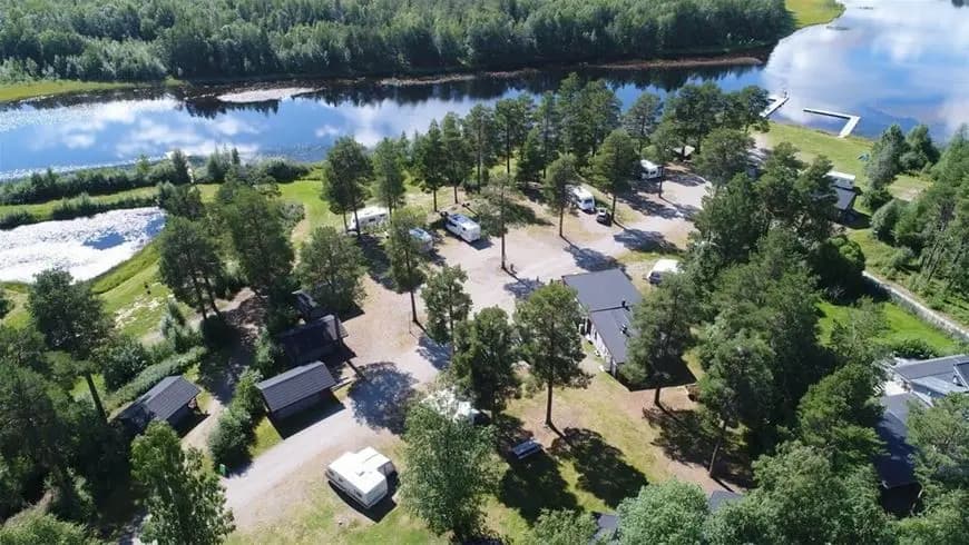 Flygfoto över Sonfjällscampen som visar ett naturskönt landskap med skog, flod och sjö.