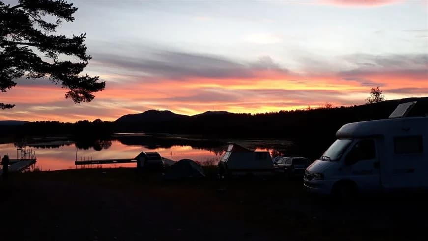 En idyllisk vy över Sonfjällscampen med en spegelblank sjö som reflekterar en himmel färgad av solnedgångens varma toner.