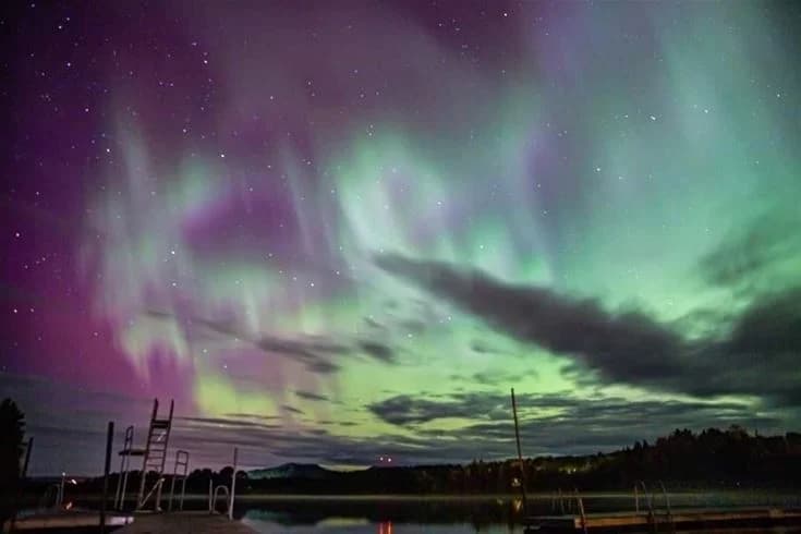 En fantastisk nattbild av Sonfjällcampen där norrskenet lyser upp den mörka himlen med stjärnorna som bakgrund.
