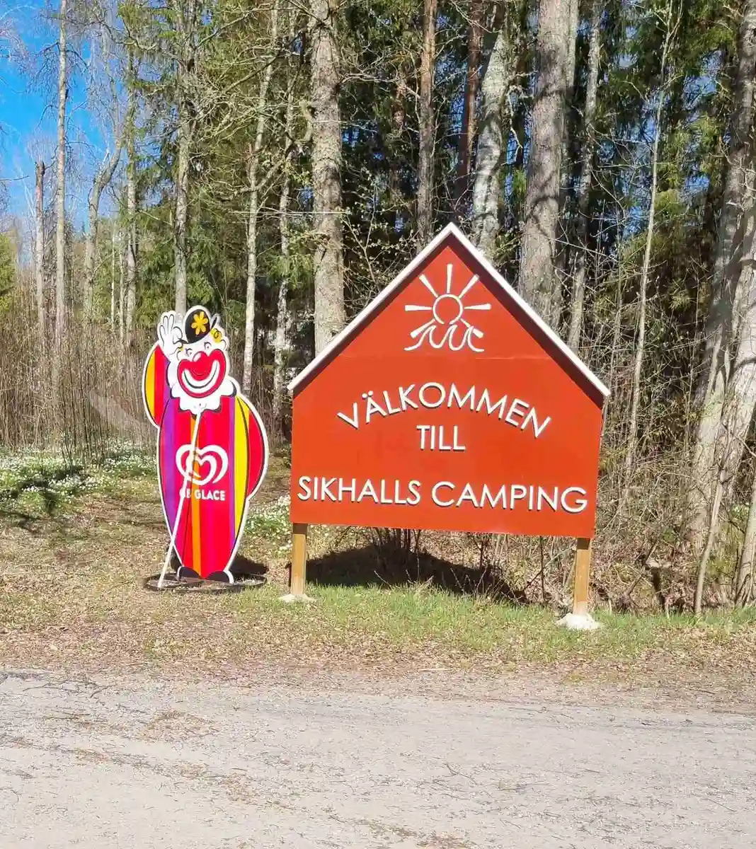 En skylt i en grönskande park vid Sikhalls Camping omgiven av tät skog.