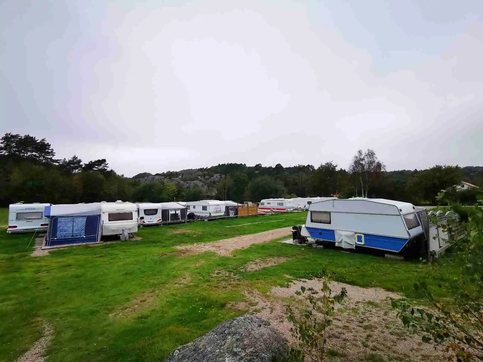 En naturskön campingplats i Hunnebostrand med husvagnar, tält och campingfordon under en klar himmel med cumulusmoln.