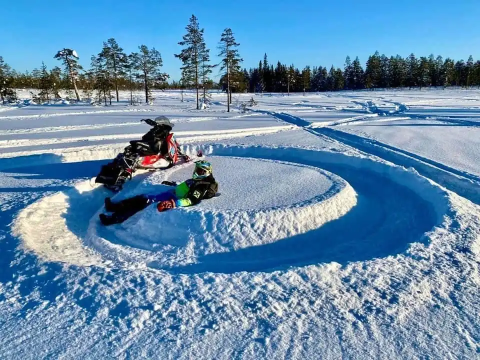 En snöskoter kör genom ett vinterlandskap täckt av djup snö, med isiga formationer och ett arktiskt klimat som omger platsen, lämplig för vintersport och äventyr.