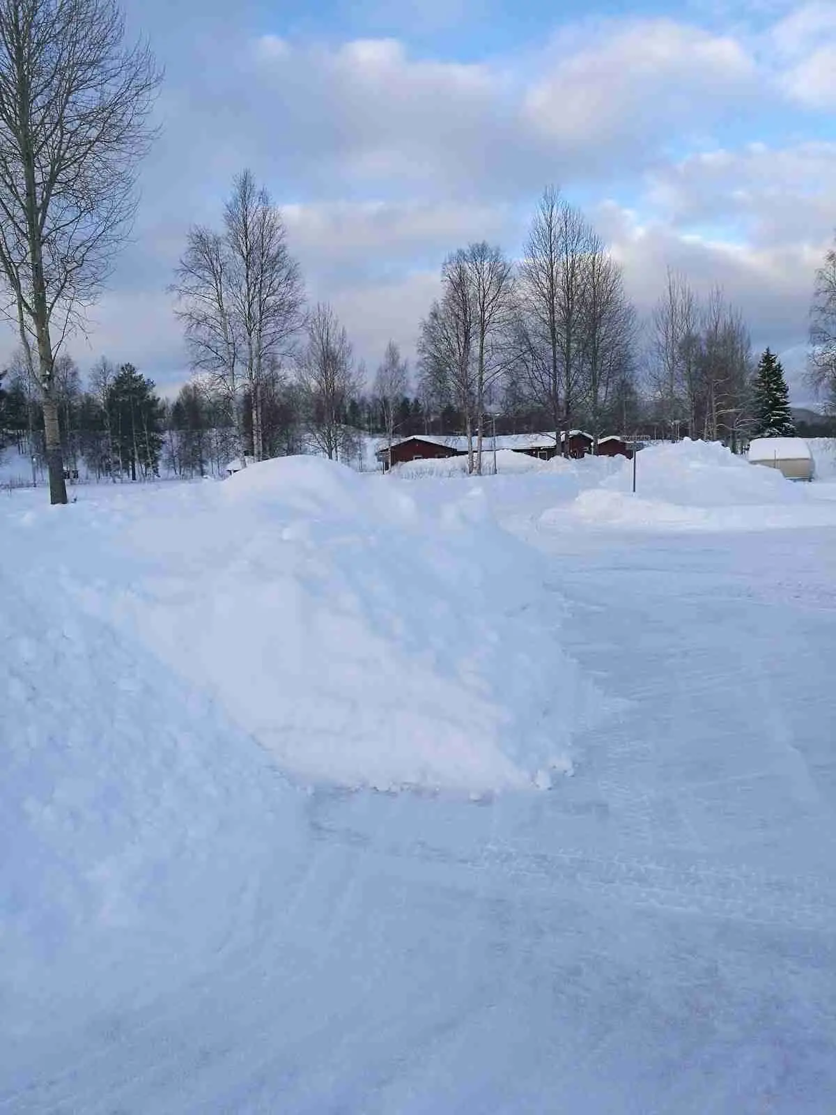 En vinterbild av Hede Camping visar snötäckt landskap under klar blå himmel, med trädgrenar som sträcker sig över den frusna marken.