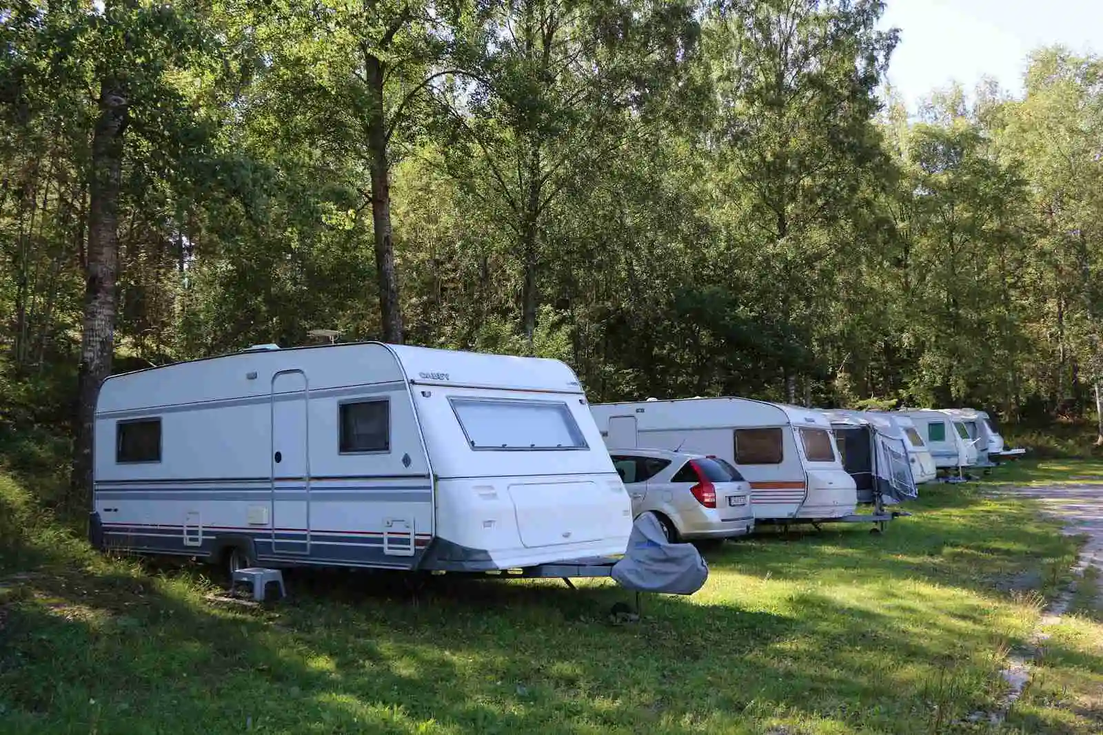 Bild av en campingplats på Rösjöbaden Camping & Stugby med flera husvagnar, husbilar och campingfordon parkerade i ett öppet område.