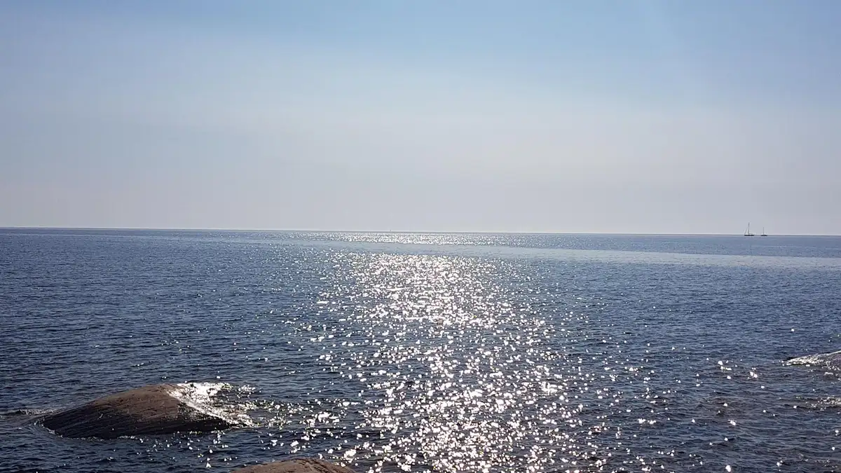 En klarblå himmel speglas i det lugna havet vid Storsands camping, där vågor försiktigt rullar in mot stranden.
