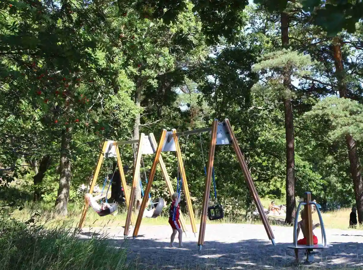 En lekplats omgiven av träd och grönska på Rösjöbaden Camping & Stugby, med en picknickyta i skuggan.