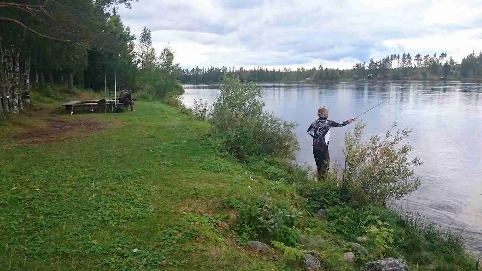 En person fiskar vid en flodbank under molnig himmel på Kvissleströmmens fiskecamping.
