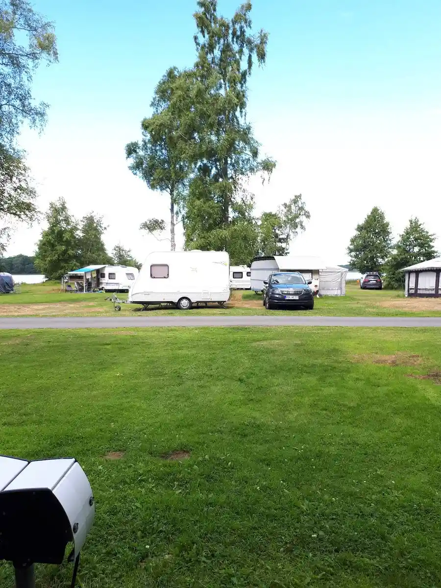 En campingplats med grönt gräs och flera husvagnar och husbilar uppställda under en molnig himmel. En lastbil ses i bakgrunden.