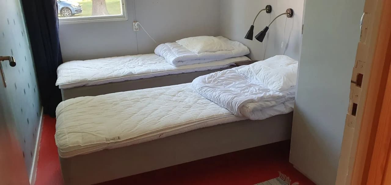 En mysig sovmiljö med en träinspirerad inredning på Stigmansgården i Tiveden. Rummet har en enkel design med en bekväm säng, trägolv och neutrala sängkläder.