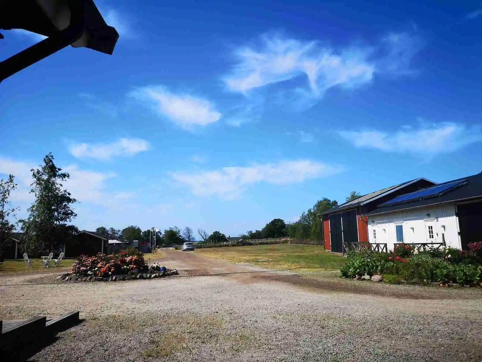 En lantlig stuga vid Rödlix Hostel & Camping med en vidsträckt äng i förgrunden. Molnen täcker himlen, och stugans uppfart skymtar i utkanten av bilden.