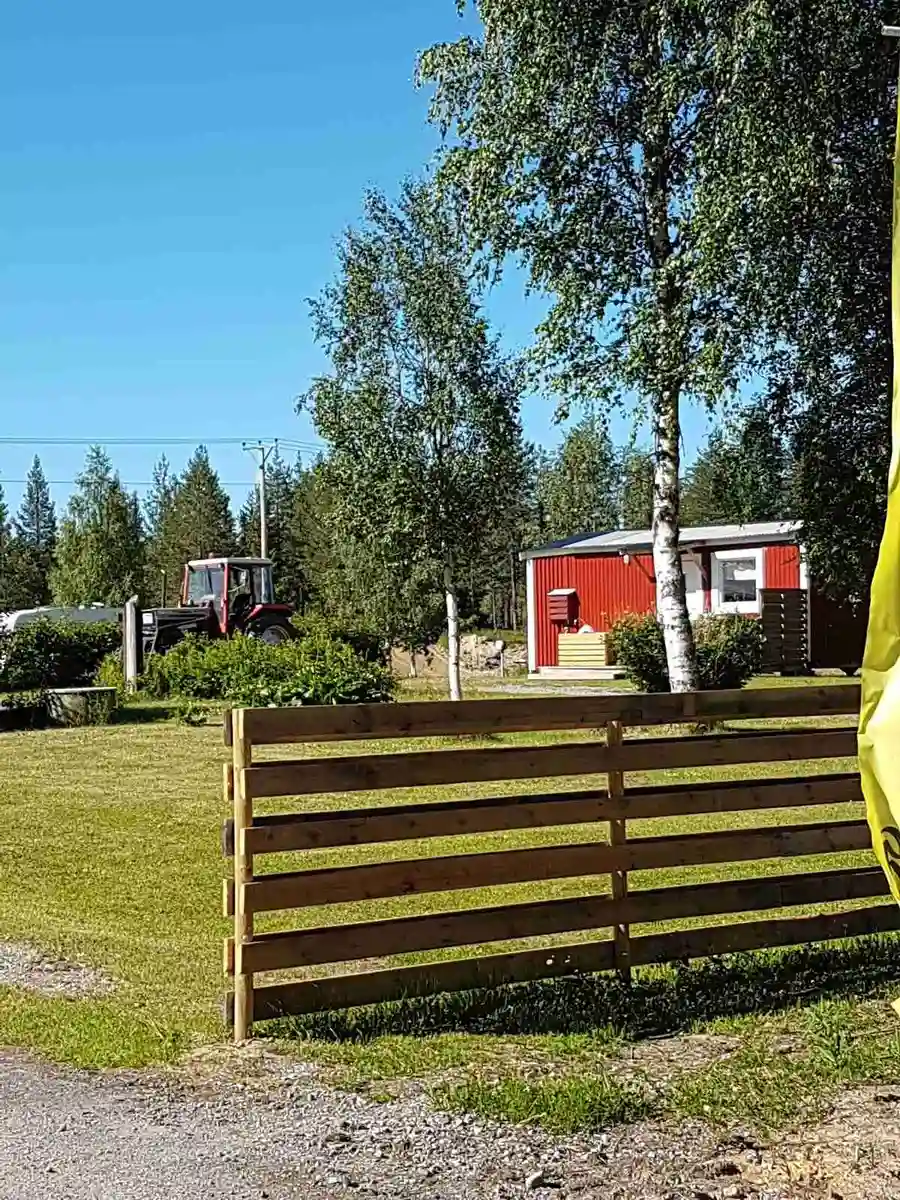 En grön gräsmatta omgiven av staket och buskage, med utsikt över ett lugnt campingområde vid Orrkulla Camping.