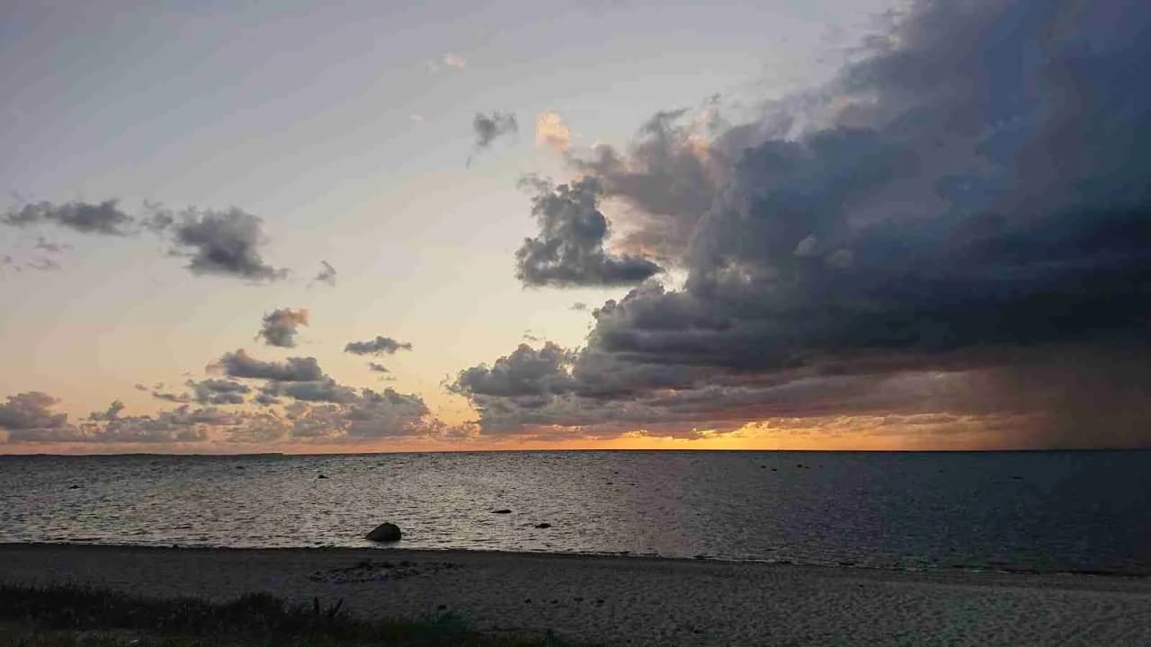 En solnedgång över stranden med himlen täckt av vita moln mot en blå horisont vid Lerbergets camping.