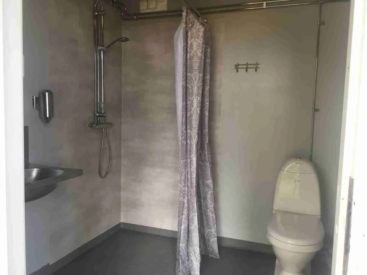 Alt-text: Interiör av ett badrum på Norraryds camping med vit kaklat golv och väggar, en toalettstol syns i förgrunden.