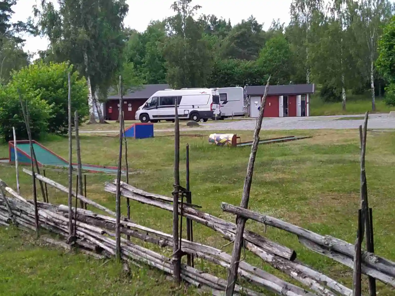 En grön campingplats vid Kapellskär med frodigt gräs och omgivande staket, omgiven av träväxtlighet och öppna marker.