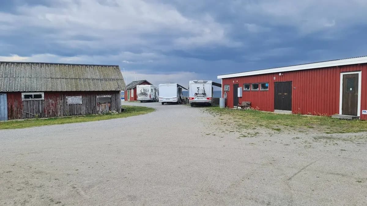 En vidsträckt utsikt över Valjevikens camping med parkering och uppställningsplatser. På bilden syns även ett mindre skjul och en uppställningsplats för lastbilar, omgiven av gräs och buskar.