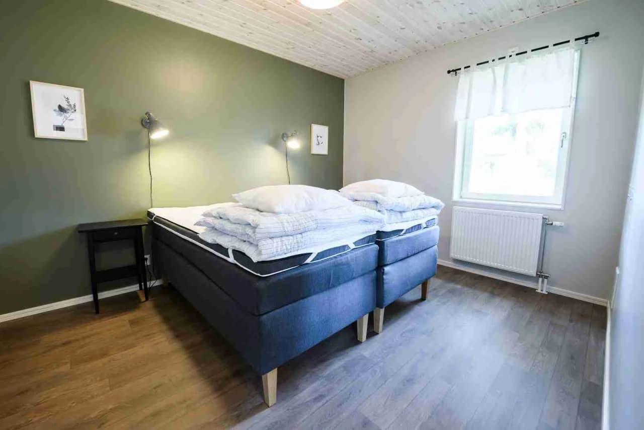 Bild av ett sovrum på Östersunds camping, med en bäddad säng, sängkläder och enkel inredning. Golvet är synligt och rummet har en ljus och välkomnande atmosfär.