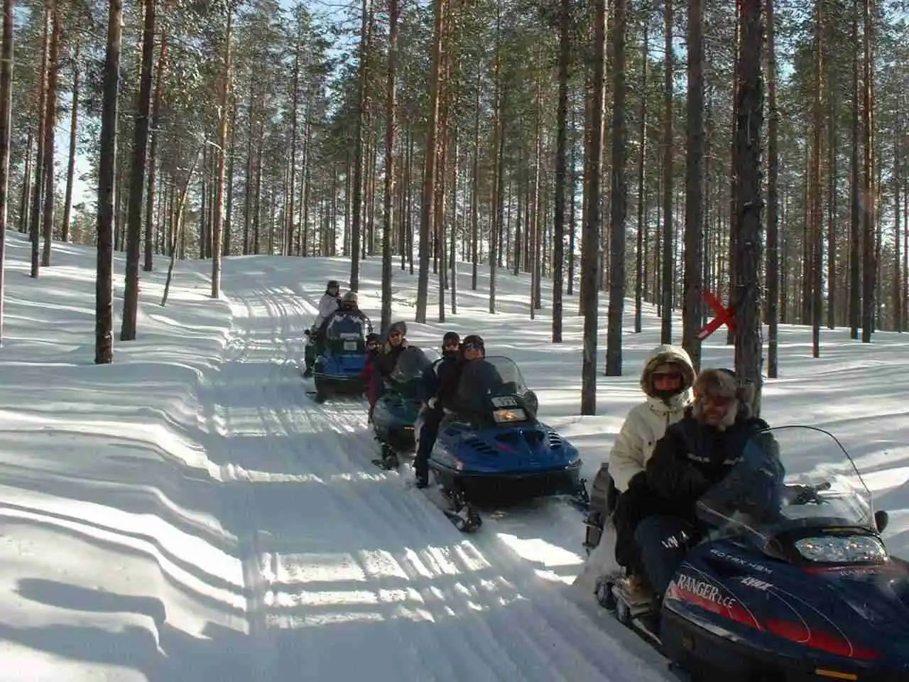 En snötäckt landskap med en snöskoter på Sörälvens fiske camping & stugby, inramad av vintriga vyer som lockar till vinteraktiviteter och äventyr. 