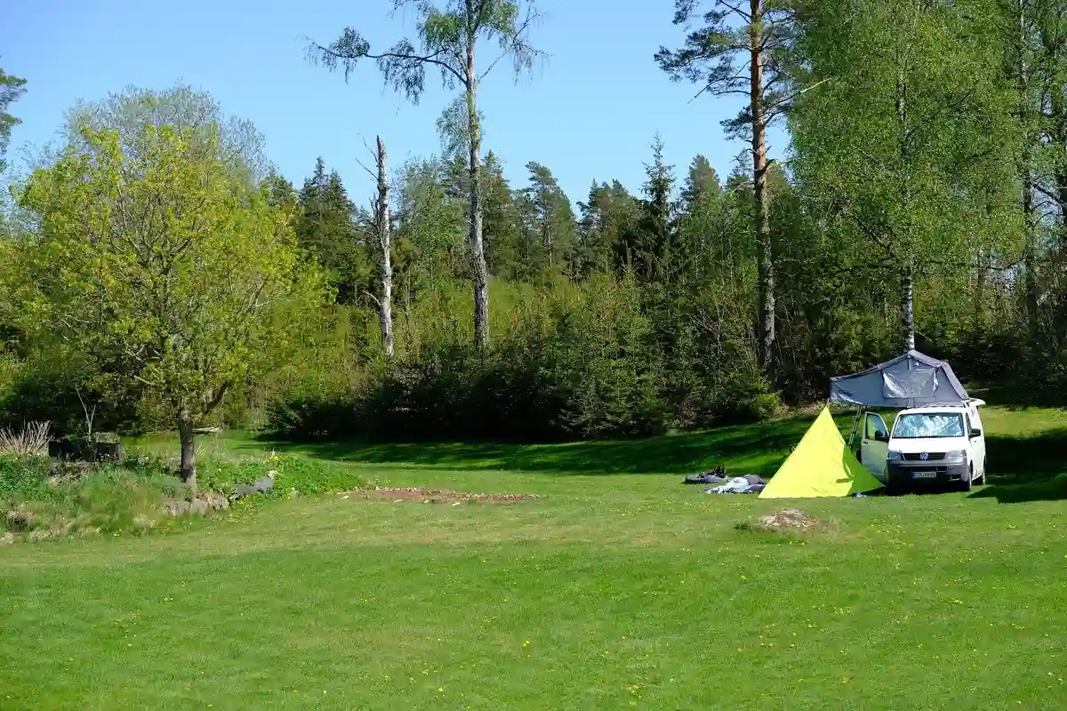 Bild av en lummig campingplats vid Ivarsbygget med grönskande träd och gräs. Flera tält är uppställda bland växtligheten, vilket ger en naturnära och avkopplande stämning.