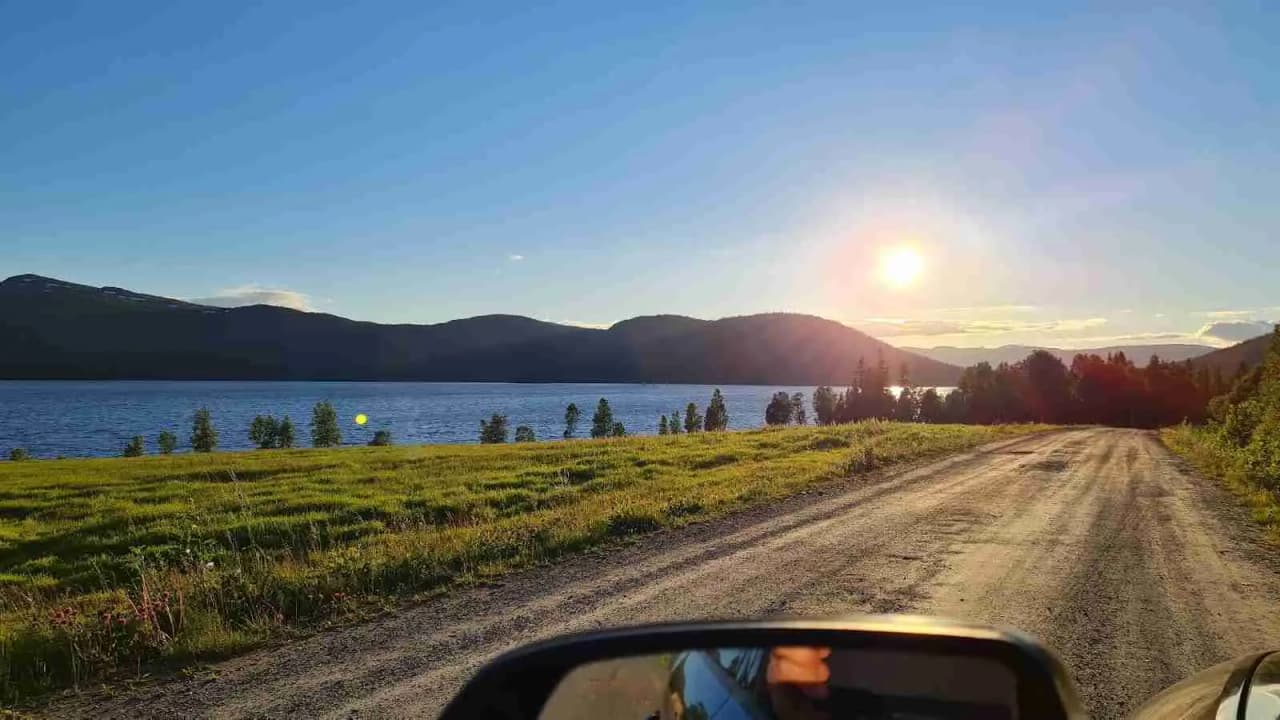 Vy över Lia Ranch Vildmarkscamping som visar en bred väg omgiven av öppet landskap och högländer. En sjö kan skymtas i horisonten under en molnig himmel.