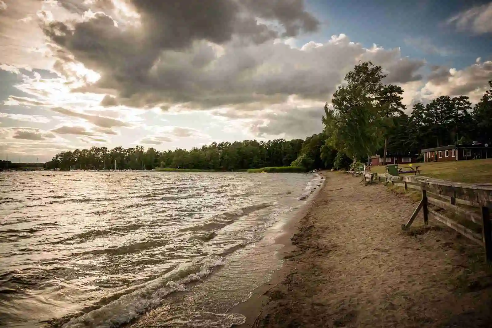 En vacker naturvy vid Bredsands bad & camping med sandstrand som sträcker sig längs kusten. Det kristallklara vattnet breder ut sig mot horisonten, inramat av en klarblå himmel med några spridda moln.