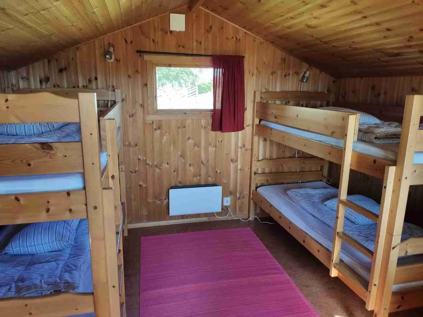 Ett trästuga på Rödlix Hostel & Camping omgiven av grönska, med robusta timmerplankor och enkla, rustika designinslag.