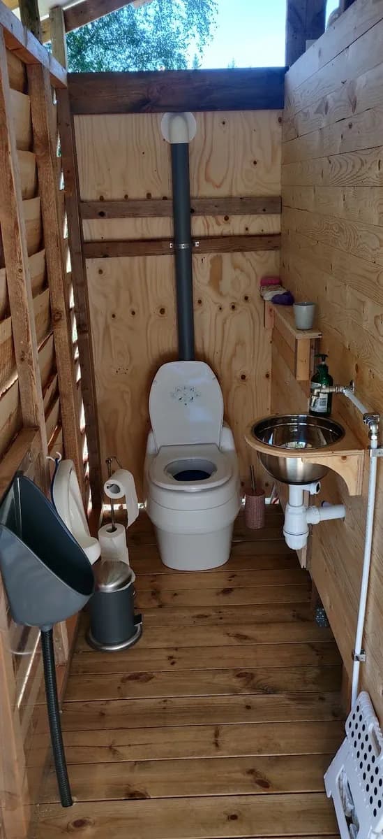 En rustik vedbyggnad med trädetaljer och enkel inredning, inklusive en toalett, på Solberg Hults camping.