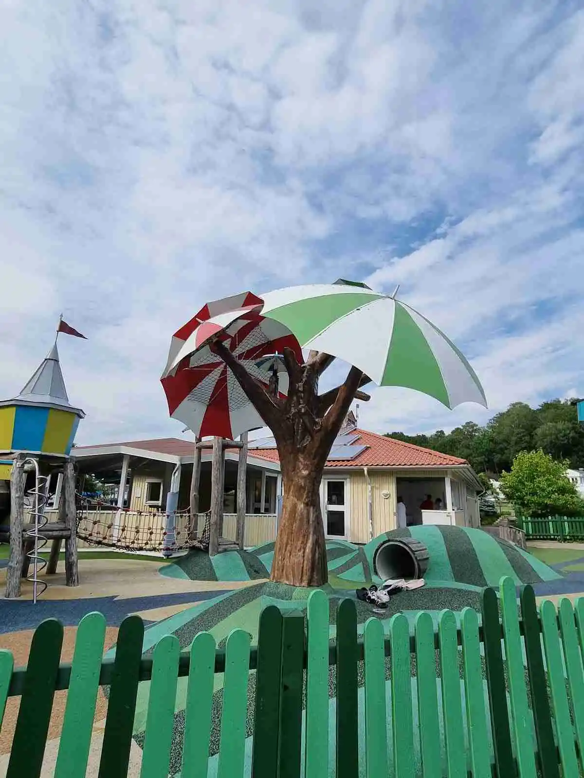 "Barn som leker på en lekplats i Lisebergsbyn, omgiven av grönska och skuggiga områden. Perfekt för rekreation och familjenöjen."