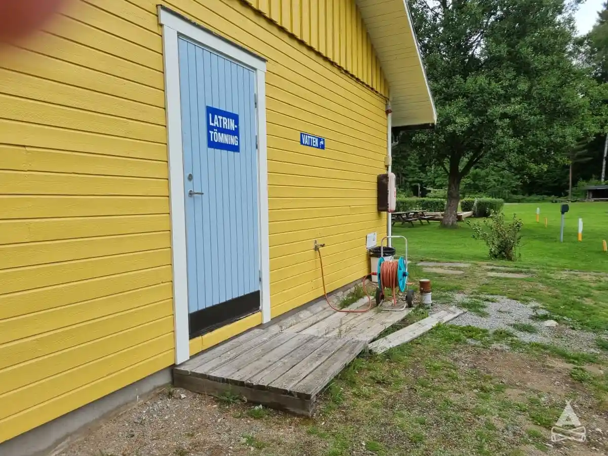 Ett litet trähus med rödmålad fasad och vit dörr, omgiven av en grönskande gård. Det ser ut som en mysig plats för övernattning på Sofielund vandrarhem & camping.