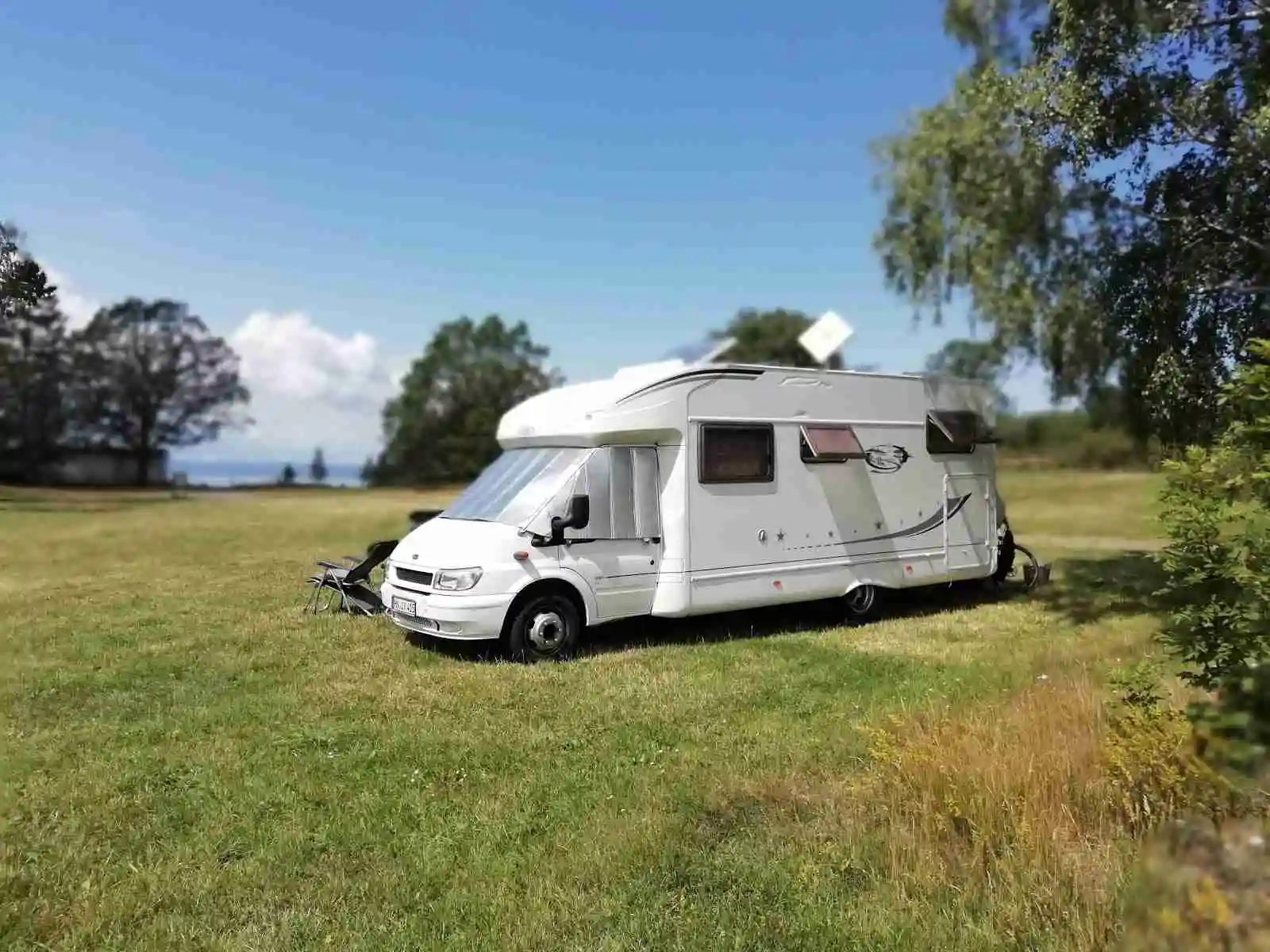 En campingplats vid Vättersmålen med flera husbilar och husvagnar uppställda. Fordonen, utrustade med backspeglar och hjulsidor, står parkerade nära varandra och omges av grönska, vilket ger en avkopplande atmosfär för campare.