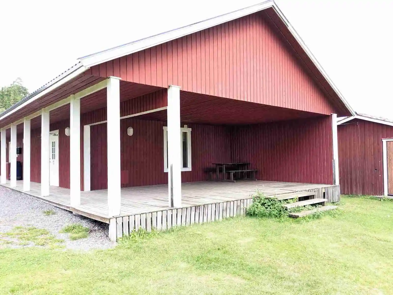 En trästuga med brunt tak och träpaneler står på en grön gräsmatta under en klar himmel, omgiven av öppet landskap på Charlottenberg camping & stugor - Haganäset.