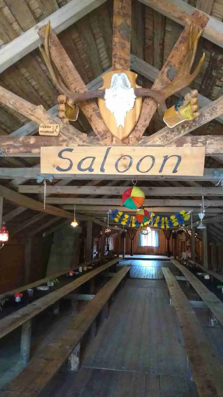 En interiör av en träbyggnad på Höljes camping, med synliga träbalkar och tak av polerade träplankor, en enkel taklampa hänger ner från taket.